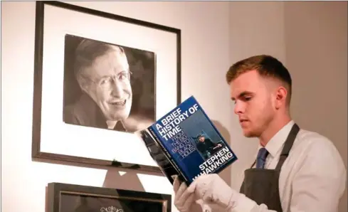  ?? DANIEL LEAL-OLIVAS/AFP ?? A gallery assistant poses with a copy of the book by theoretica­l physicist Stephen Hawking signed with a thumbprint during a photocall for the sale of personal items from Hawking’s estate at Christie’s auction house in London on Tuesday.