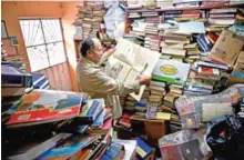  ??  ?? Jose Alberto Gutierrez reads an old newspaper among books stacked in his library.