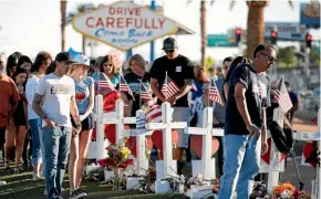  ??  ?? People gather in Las Vegas yesterday to look at white crosses set up for the victims of the mass shooting.