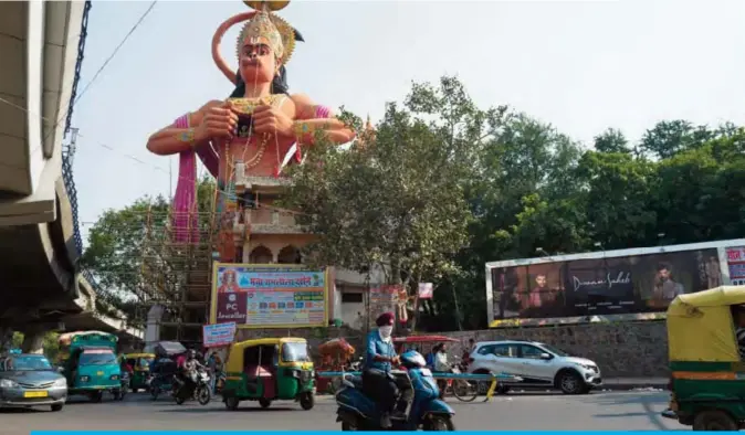  ?? — AFP ?? NEW DELHI: A motorist (C) wearing a face mask for protection against air pollution rides past an idol of Hindu god Hanuman.
