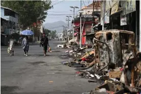  ?? Photograph: Arun Sankar/AFP/Getty ?? People walk past a burnt vehicle and rubble in Churachand­pur in violence-hit areas of the north-eastern Indian state of Manipur on 9 May.
Images