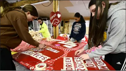  ?? JENNY SPARKS — REPORTER- HERALD ?? Thompson Valley High School students Charlotte Wright, 15, left, Kate Weimer, 15, right, and Inezya Wilson, 15, center, tape stencils with messages of love to wooden hearts before painting them Wednesday.