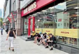  ?? ?? Delivery workers sit outside Five Guys, a fast-food restaurant which has closed its streetside door. — Zhu Shenshen