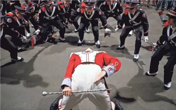  ?? ?? Members of the band’s B-row cheer as Austin Bowman does his third backbend during the “Three Knocks” tradition signaling the arrival of the band at the stadium.