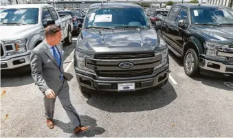  ?? Steve Gonzales / Houston Chronicle ?? Sterling McCall general manager Frank Pierce walks by a row of Ford F-150 pickup trucks. The popular trucks start at $27,700 but a decked-out F-150 can run more than $70,000.