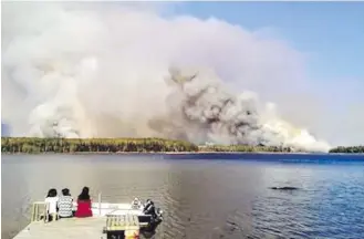  ?? CLINTON KEPER, THE CANADIAN PRESS ?? People from the Paungassi First Nation watch a fire burning in Little Grand Rapids, Man., about 260 kilometres northeast of Winnipeg. About 1,400 people are to be evacuated from two First Nations communitie­s.