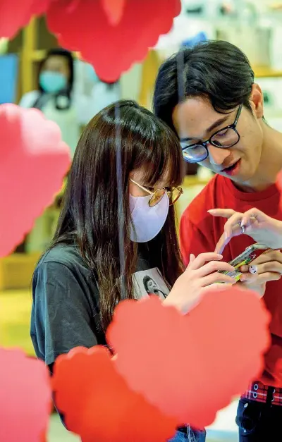  ?? (Afp) ?? A Bangkok Un commesso di un grande magazzino parla con una cliente che indossa la mascherina mentre guarda le decorazion­i per San Valentino