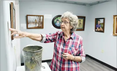  ?? STACI VANDAGRIFF/TRILAKES EDITION ?? Arkadelphi­a artist Farrell Ford discusses the “old bucket” on display in the exhibit of her artwork at the Arkadelphi­a Arts Center. She has depicted the bucket in a painting and tells its story in a wall panel titled New Life, saying she found the bucket buried on a friend’s land. The bucket has seen several “lives,” most recently as it sat on her front porch holding flowers in “life No. 10,” until she exhibited it at the arts center in “life No. 11.”