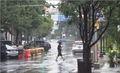  ?? Tyler Sizemore / Hearst Connecticu­t Media ?? A pedestrian crosses the street with an umbrella as Tropical Storm Henri hits Stamford on Sunday. Henri was downgraded from a hurricane to a tropical storm as the storm took a turn eastward before hitting land.