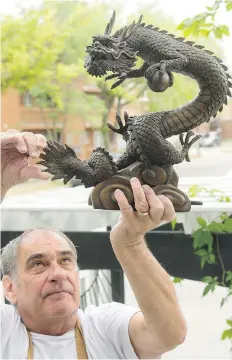  ?? MICHAEL BELL ?? Rick Urbanski holds up a bronze dragon at the entrance to his business, Dragon’s Nest B&B. Late Wednesday night or early Thursday morning, an identicall­y shaped but much larger version of the dragon statue was stolen from the entrance to the property.