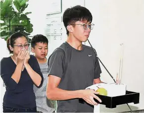  ?? — Bernama ?? Family in grief: Ng’s wife Loh Hwa Hong and her youngest child Chin Khai accompanyi­ng 17-year-old Chin Wee as they make prayer offerings during the wake for Ng. Right: A relative paying his last respects.