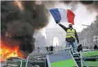  ?? MICHEL EULER/ ASSOCIATED PRESS ?? A demonstrat­or waves the French flag while standing on a burning barricade near the Arc de Triomphe in Paris during Saturday’s demonstrat­ion against rising fuel taxes and the perceived elitism of France’s ruling class.