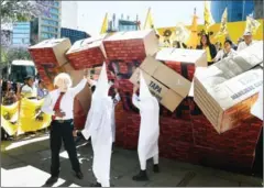  ?? ALFREDO ESTRELLA/AFP ?? Mexicans wearing a mask of US President Donald Trump and dressed as Ku Klux Klan members build a symbolic wall to protest in front of the US Embassy in Mexico City on February 20.