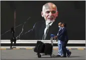  ?? RAHMAT GUL — THE ASSOCIATED PRESS FILE ?? Passengers walk to the departures terminal of Hamid Karzai Internatio­nal Airport in Kabul, Afghanista­n, on Saturday, past a mural of President Ashraf Ghani, as the Taliban offensive encircled the capital.
