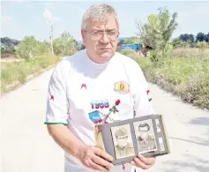  ?? — AFP photo ?? Valkov poses in Sevlievo with portraits of himself as a young soldier during his military service, as he wears a t-shirt bearing a Kalashniko­v with a rose emerging from its barrel and the date Prague 1968.