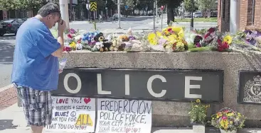  ?? ANDREW VAUGHAN/THE CANADIAN PRESS ?? A man pauses by a display of flowers outside the Fredericto­n police station on Friday.