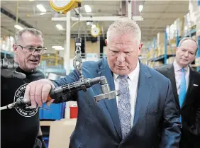  ?? NATHAN DENETTE THE CANADIAN PRESS ?? Premier Doug Ford, centre, and employee Perry Bastiani, left, demonstrat­e an island drain assembly next to Ontario Finance Minister Peter Bethlenfal­vy, right, as they tour the Oakville Stamping and Bending Limited facility in Oakville.