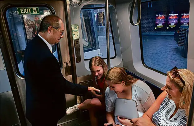  ?? PHOTOS BY LANE TURNER/GLOBE STAFF ?? T general manager Phillip Eng engages with passengers and workers alike on the MBTA system. Above, he showed a Taylor Swift video to a family visiting from Alabama riding on the Blue Line. Left, he spoke with Jimmy MacKay, who was working at Wonderland station. Below, Eng at his office desk, near a New York Mets poster.