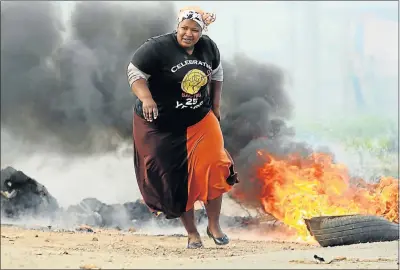  ?? Picture: EUGENE COETZEE ?? FIERY BARRICADE : A woman evades tyres set alight by protesters who closed the old Missionval­e Road yesterday