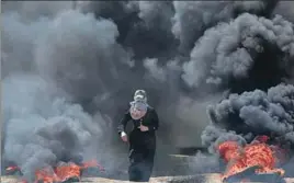  ?? AP ?? ■ A Palestinia­n woman walks through smoke from burning tires during a protest at the Gaza Strip.