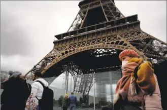 ?? Christophe Ena / Associated Press ?? A woman wearing a mask walks past the Eiffel Tower, which was closed after the French government banned all gatherings of over 100 people to limit the spread of the virus COVID-19, in Paris on Saturday.