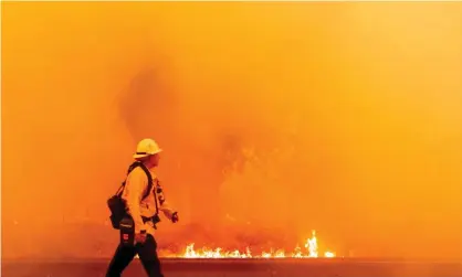  ?? Photograph: Josh Edelson/AFP/Getty Images ?? A Pacific Gas and Electric firefighte­r walks down a road as flames approach in Fairfield, California, on 19 August.