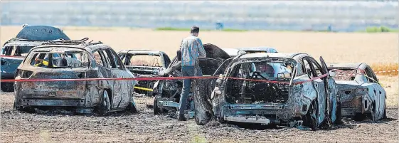  ?? BOB TYMCZYSZYN THE ST. CATHARINES STANDARD ?? An investigat­or examines wreckage of a fire that caused more than $1 million damage to vehicles parked in a dry field Sunday for the Niagara Lavender Festival.