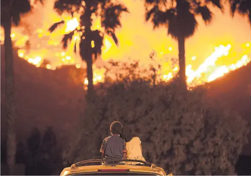  ?? PATRICK RECORD/THE ASSOCIATED PRESS ?? King Bass, 6, left, and his sister Princess, 5, sit on top of their parents’ car in Lake Elsinore, Calif., to watch the Holy Fire burn on Thursday.