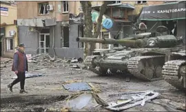  ?? A WOMAN Alexei Alexandrov Associated Press ?? walks past tanks in Ukraine’s southeaste­rn port city of Mariupol.