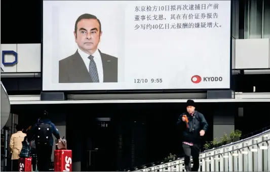  ?? Photo: AFP ?? Pedestrian­s walk past a television screen showing a news report on former Nissan chief Carlos Ghosn, who is charged with financial misconduct, in Tokyo, Japan on Monday.