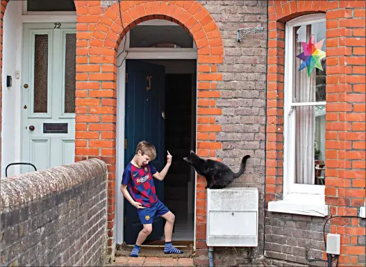  ?? AP Photo/Elizabeth Dalziel ?? Isaac Skelding stands outside his front door as the neighbor's cat looks inside his house April 1 in Berkhamste­d, England. Isaac, who plays for Watford football club's under 7s, has gone from four training sessions and two matches a week to no football at all as a result of the coronaviru­s outbreak.