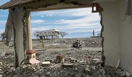  ??  ?? Still lots to be done: (Top) A motorist riding past ruins of buildings destroyed by the earthquake while (left) two women are chatting among tents at a temporary shelter in Palu.