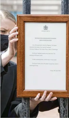  ?? Foto: Ian West/PA Wire, dpa ?? Freitagmit­tag in London: Eine Mitarbeite­rin hängt eine Tafel mit der Todesmitte­ilung an das Tor des Buckingham‰Palasts.