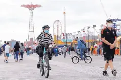  ?? KATHY WILLENS/ASSOCIATED PRESS ?? A woman rides her bicycle Sunday on the boardwalk at Coney Island in New York. Memorial Day weekend is usually marked by large gatherings, and health officials have implored people to avoid risky behavior.