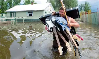  ?? THE CANADIAN PRESS/JONATH AN HAYWARD ?? Resident Lars Androsoff carries his friend's guitars as he walks through the floodwater­s in Grand Forks, B.C., on Thursday.