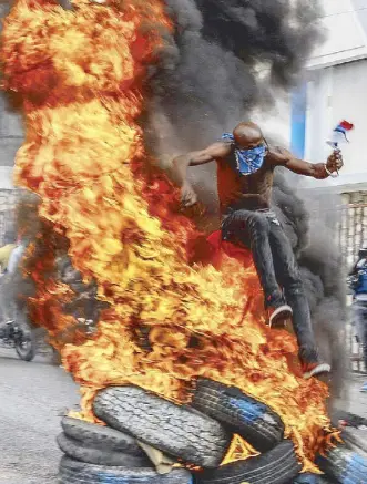  ?? AP ?? A demonstrat­or jumps over burning tires during a protest against Haitian Prime Minister Ariel Henry in Port-au-Prince on Monday.