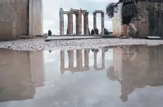  ??  ?? From left: Tourists are reflected in a large puddle as they walk past the ancient Temple of Zeus, after rainfall, in central Athens; a man looks on waves in the southern Athens seaside suburb of Flisvos.