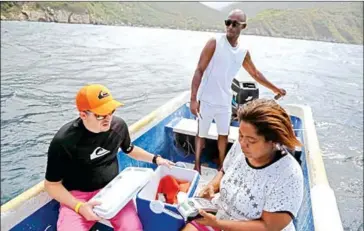  ?? FEDERICO PARRA/AFP ?? Rodriguez (right) charges food to a tourist’s credit card in a boat, after motoring 2 kilometres off the coast of Chichirivi­che de la Costa, to find an internet signal on January 13.