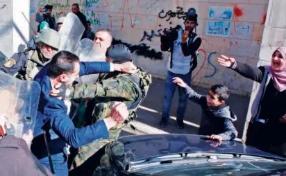  ?? Agence France-presse ?? A Palestinia­n woman (top) shields her injured husband as security forces scuffle with him (right) during a rally of Hamas supporters in the occupied West Bank town of Hebron on Friday.