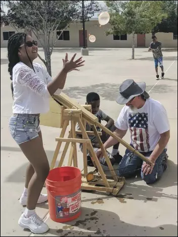  ?? JULIE DRAKE/Valley Press ?? Lancaster School District student Lucy Chaney (left) reaches up to catch a couple of water balloons Monday as teacher Chris Becker (right) explains a trebuchet to student J’quan Knight.