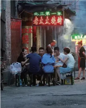  ??  ?? People eat chuan’r on the street as a waitress waits for orders