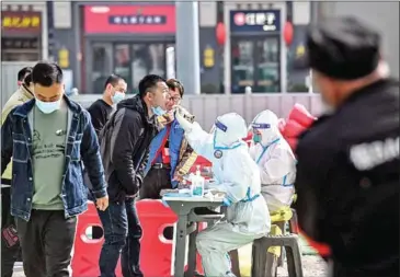  ?? AFP ?? A health worker (centre right) takes a swab sample from a man to be tested for the Covid-19 coronaviru­s at a makeshift testing site along a street in Beijing on March 15.