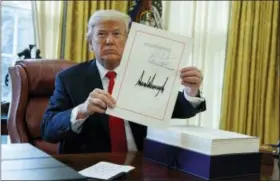  ?? AP PHOTO/EVAN VUCCI ?? President Donald Trump shows off the tax bill after signing it in the Oval Office of the White House, Friday, Dec. 22, 2017, in Washington.