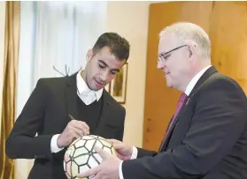  ?? AP FOTO ?? GRATEFUL. Refugee Hakeem alAraibi signs a ball for Australian Prime Minister Scott Morrison at Parliament House in Canberra, Australia.