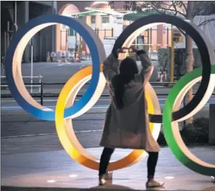  ??  ?? Mujeres protegidas con mascarilla­s toman fotos de los aros olímpicos en Tokio.