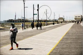  ?? MATT ROURKE — THE ASSOCIATED PRESS FILE ?? FILE – In this April 28, 2020, file photo, a person, wearing a protective face mask as a precaution against the coronaviru­s, walks with their phone on the sparsely occupied boardwalk in Atlantic City, N.J. New Jersey launched a website to debunk rumors and hoaxes associated with the spread of the coronaviru­s, following a false text message of impending national lockdown that circulated widely across the United States.