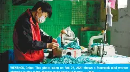  ??  ?? WENZHOU, China: This photo taken on Feb 27, 2020 shows a facemask-clad worker stitching insoles at the Zhejiang Xuda Shoes Co factory. — AFP