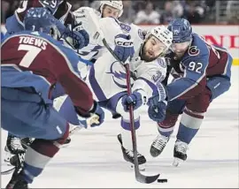  ?? John Locher Associated Press ?? BRANDON HAGEL of the Lightning reaches for the puck between Avalanche players Devon Toews (7) and Gabriel Landeskog during the first period of Game 1.
