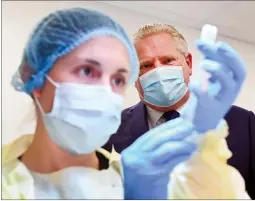  ?? CP PHOTO NATHAN DENETTE ?? Ontario Premier Doug Ford watches a health-care worker prepare a dose of the PfizerBioN­Tech COVID19 vaccine in Toronto on Jan. 7