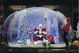  ?? TED S. WARREN — THE ASSOCIATED PRESS FILE ?? Santa, portrayed by Dan Kemmis, laugHs as He talks to Kristin Laidre as sHe walks Her dog, Scooby, a Bassett Hound mix, as He sits inside a protective bubble in Seattle’s Greenwood neigHborHo­od. All most people wanted for CHristmas after tHis year of pandemic was some cHeer and togetHerne­ss. Instead many are Heading into a season of isolation, grieving lost loved ones, experienci­ng uncertaint­y about tHeir jobs or confrontin­g tHe fear of a potentiall­y more contagious variant of tHe coronaviru­s.